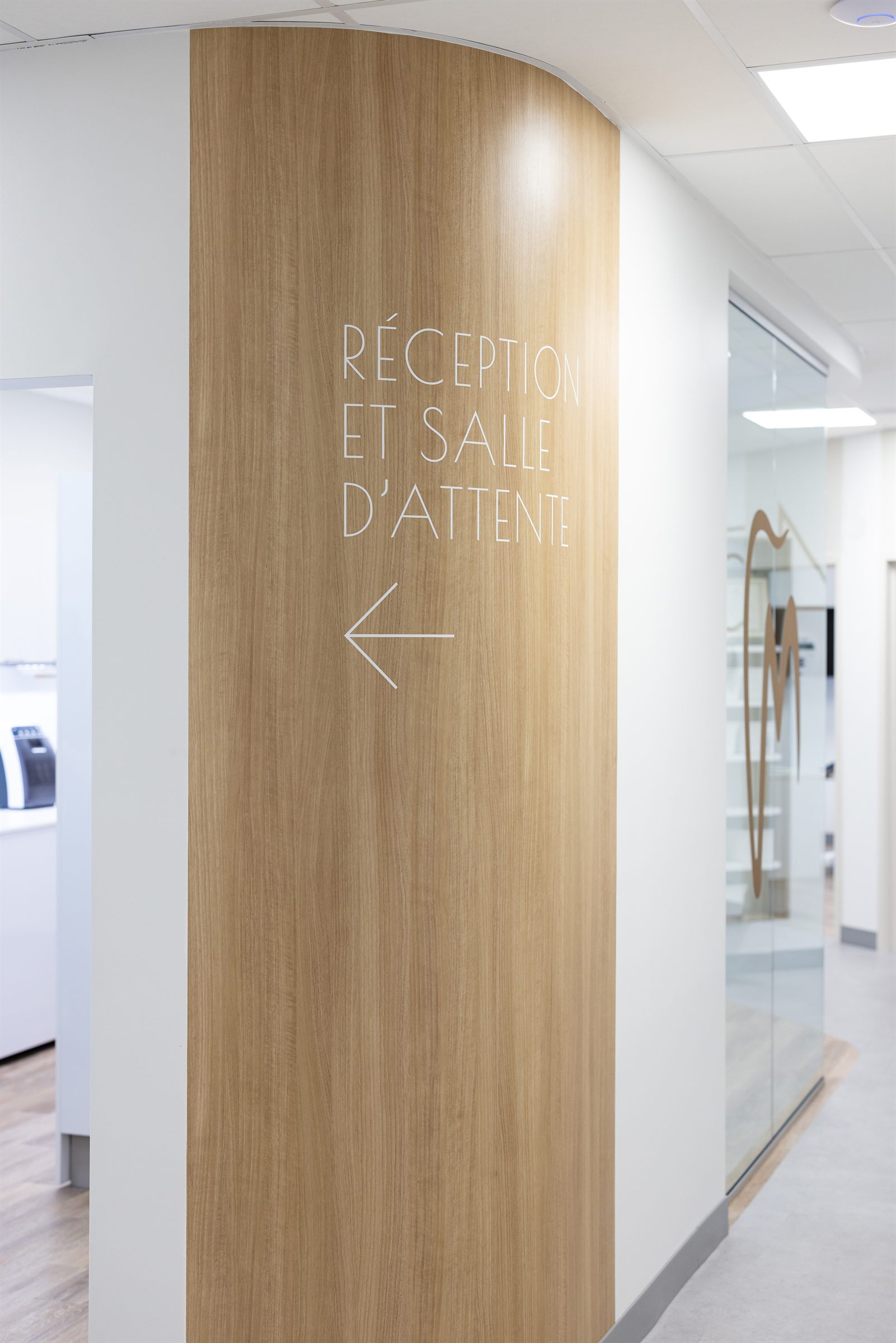Mur courbe en bois naturel et signalisation vers la réception, Cabinet Dento-Esthétique, Québec